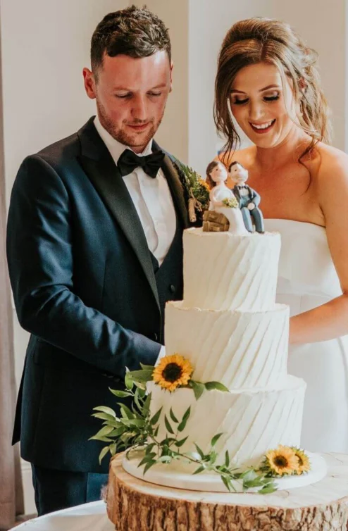 A couple joyfully cuts a tiered wedding cake decorated with sunflowers at Hastings Hotel.