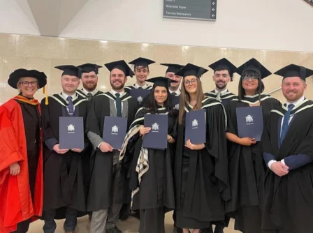 A joyful group of graduates in caps and gowns celebrate together indoors.