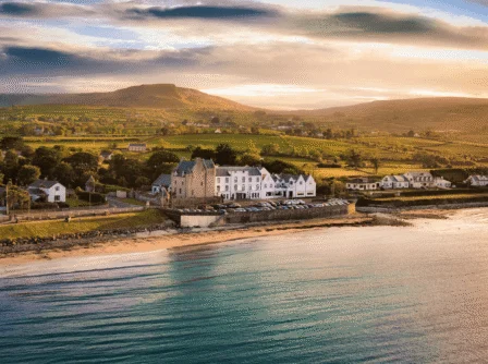 Scenic coastal view of Hastings Hotels at sunset with lush hills and serene beach.