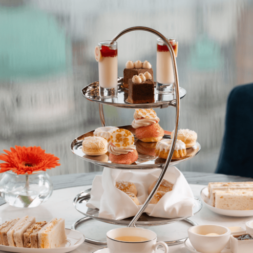 Elegant afternoon tea with pastries and sandwiches on a table in a cosy hotel setting.