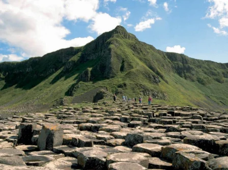 Family exploring Giant's Causeway with lush green mountains under a bright blue sky.
