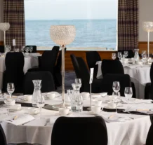 Elegant dining room with ocean view, set for an event with round tables and crystal lamps.