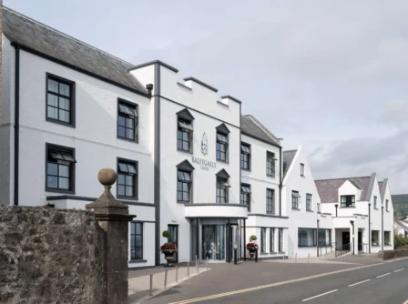 Elegant white hotel exterior with flowers, inviting entrance, and clear road view.