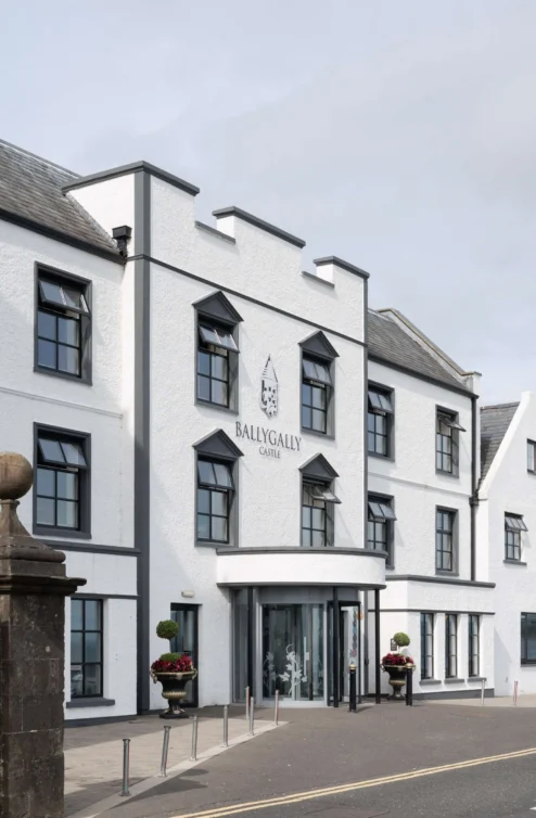Elegant white hotel exterior with flowers, inviting entrance, and clear road view.