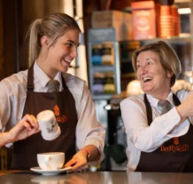 Two smiling staff members at Ballygally Castle serving drinks at a cosy bar.