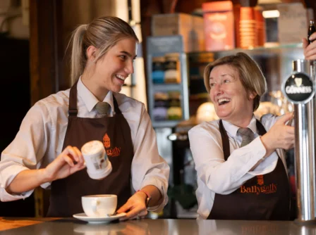 Two smiling staff members at Ballygally Castle serving drinks at a cosy bar.
