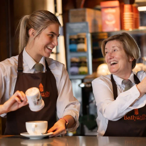Two smiling staff members at Ballygally Castle serving drinks at a cosy bar.