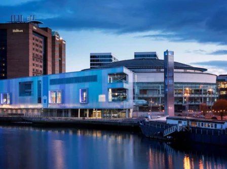 Evening view of riverside hotel and modern architecture, reflecting warm lights on water.