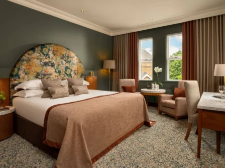 Elegant hotel room with a large bed, cosy chairs, and a scenic window view.