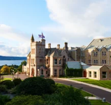 A picturesque view of a grand hotel by the lakeside, surrounded by lush greenery.