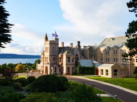 A charming hotel by the sea on a sunny day, surrounded by lush greenery and blue skies.