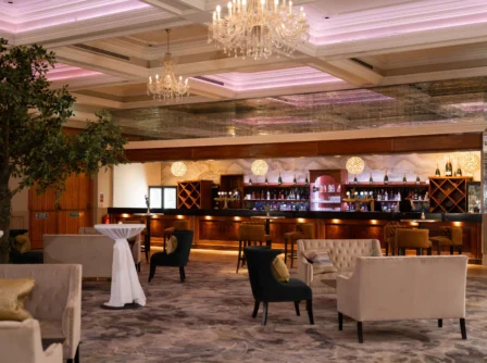Elegant hotel lounge with plush seating and a well-stocked bar under a sparkling chandelier.