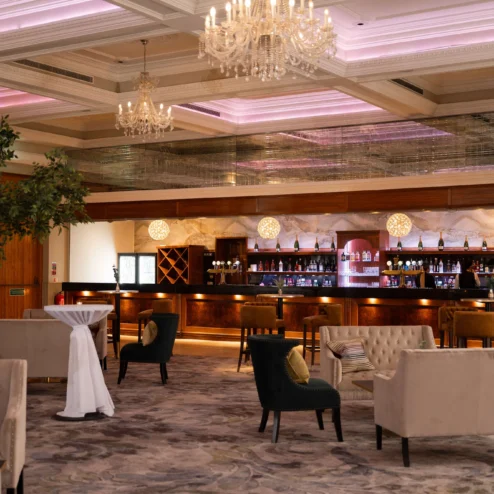 Elegant hotel lounge with plush seating and a well-stocked bar under a sparkling chandelier.