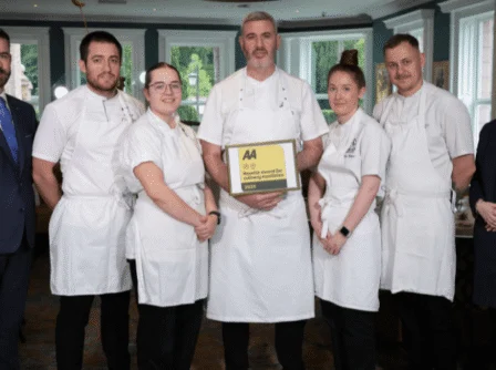 A welcoming group of chefs and staff in a cosy, elegant restaurant setting, holding an award.