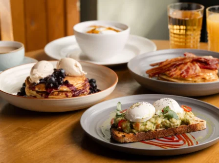 Hotel breakfast spread with eggs, pancakes, and drinks on a wooden table.