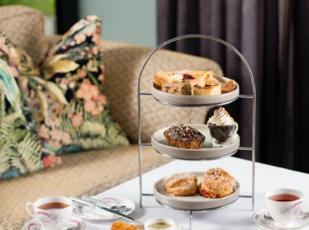 Afternoon tea setup with pastries on a tiered stand beside a cosy sofa.