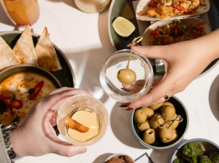 A couple toasts over a tempting array of tapas and drinks at a stylish restaurant table.