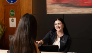 Hotel receptionist greeting guest at check-in with warm artwork behind them.