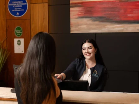 Hotel receptionist greeting guest at check-in with warm artwork behind them.