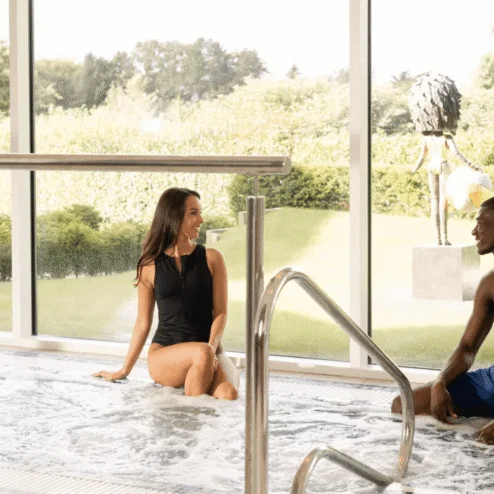 Couple enjoying a relaxing dip in a hotel's indoor jacuzzi with a garden view.
