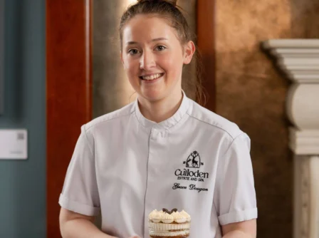 Smiling Culloden chef holding a dessert in a warm, elegant restaurant setting.