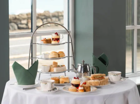 Elegant afternoon tea spread by a large window with treats and warm sunlight.
