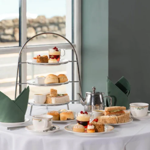 Elegant afternoon tea spread by a large window with treats and warm sunlight.
