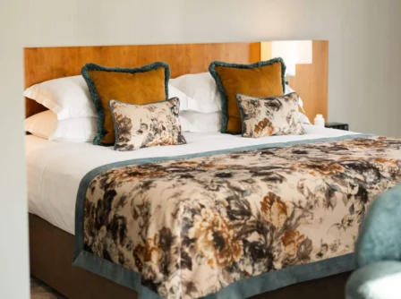 Elegant hotel room with a large bed, floral bedding, and warm lighting.