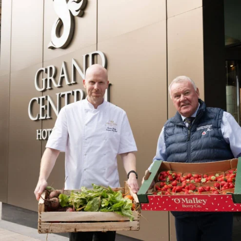 Two men holding fresh produce outside Grand Central Hotel, Belfast.
