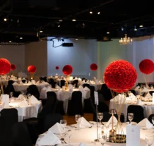Elegant banquet hall with red rose centrepieces and round tables set for an event.