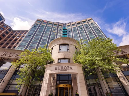 Elegant hotel facade with lush trees under a bright blue sky.