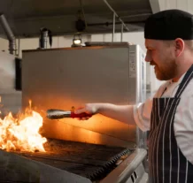 Chef grilling food over flames in a hotel kitchen, creating a warm, inviting atmosphere.