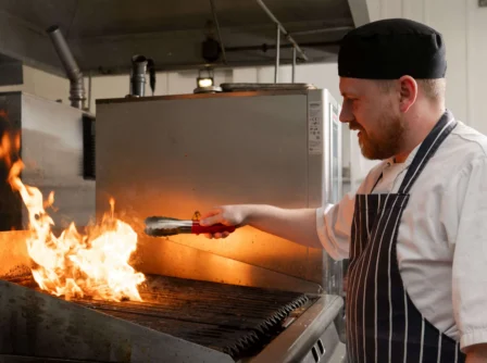 Chef grilling food over flames in a hotel kitchen, creating a warm, inviting atmosphere.