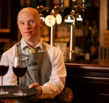 Friendly hotel staff serving red wine at a cosy bar.