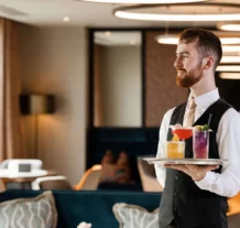 Friendly waiter serves cocktails in elegant hotel lounge.