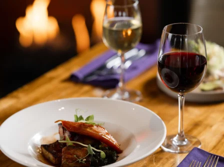 Cosy dining by the fireplace with plated gourmet meal and wine at Hastings Hotels.
