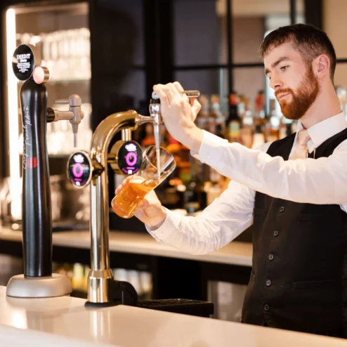 Friendly bartender pouring a draft beer in a hotel bar, surrounded by elegant decor.