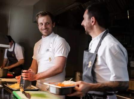 Chefs in a hotel kitchen preparing dishes, smiling and engaging warmly.