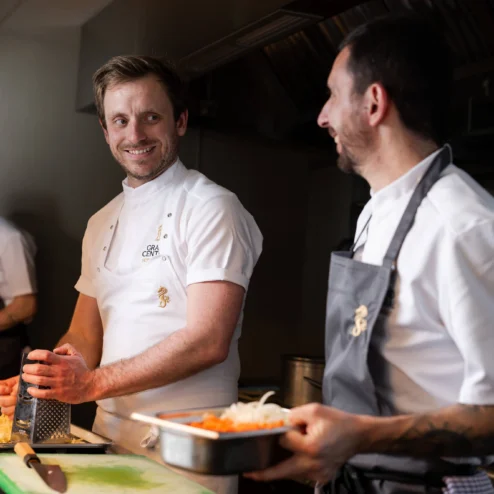 Chefs in a hotel kitchen preparing dishes, smiling and engaging warmly.
