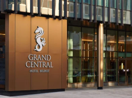 Family entering Grand Central Hotel Belfast, modern glass facade with golden accents.