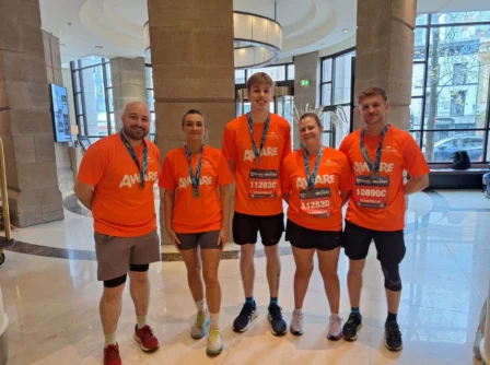 Group in orange shirts with medals, celebrating at Hastings Hotel lobby.