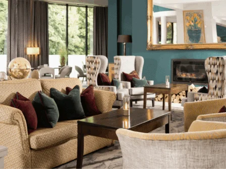 Elegant hotel lounge with cosy armchairs, a couple enjoying drinks, and a warm fireplace.