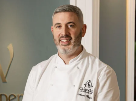 Chef smiling warmly at hotel restaurant entrance.