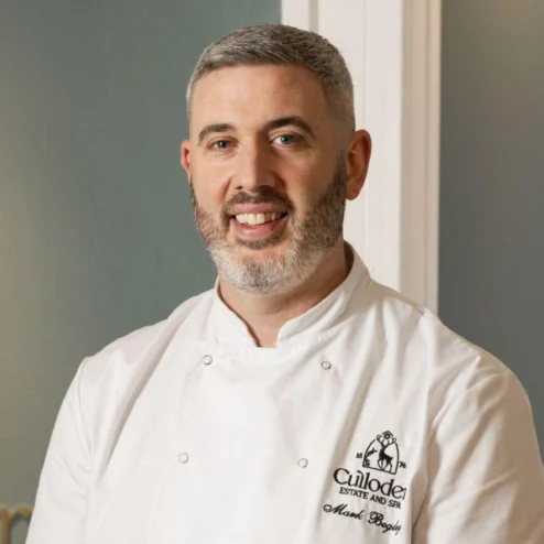 Chef smiling warmly at hotel restaurant entrance.