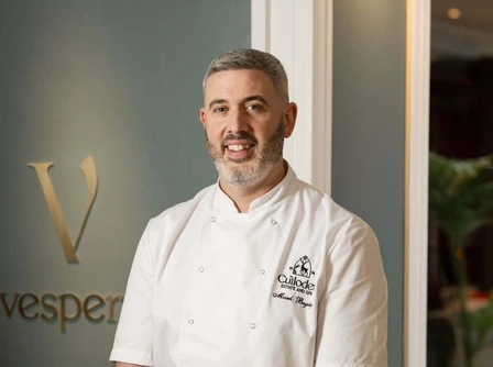 Chef smiling warmly in elegant hotel restaurant setting.