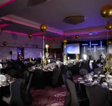 Elegant hotel ballroom set for a festive dinner event with gold balloons and ambient lighting.