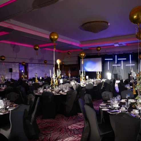 Elegant hotel ballroom set for a festive dinner event with gold balloons and ambient lighting.