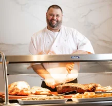 Chef carving roast meats at a hotel buffet, smiling warmly.