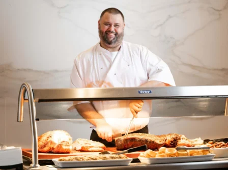 Chef carving roast meats at a hotel buffet, smiling warmly.