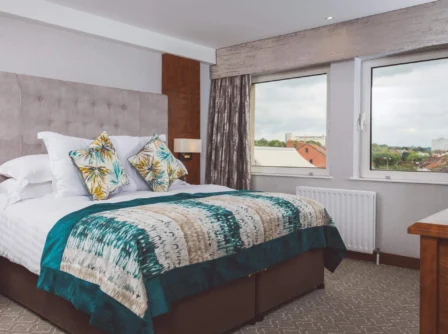 Elegant hotel room with a cosy bed and city view from large windows.